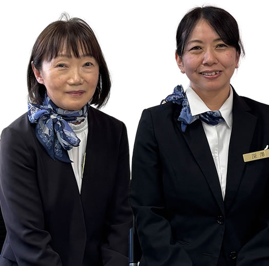 Two women in black suits and blue scarves posing against a white background, one with a name badge on her lapel (professional staff photo).