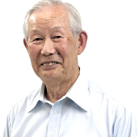 Smiling older man with gray hair wearing a light blue button-down shirt, facing the camera.