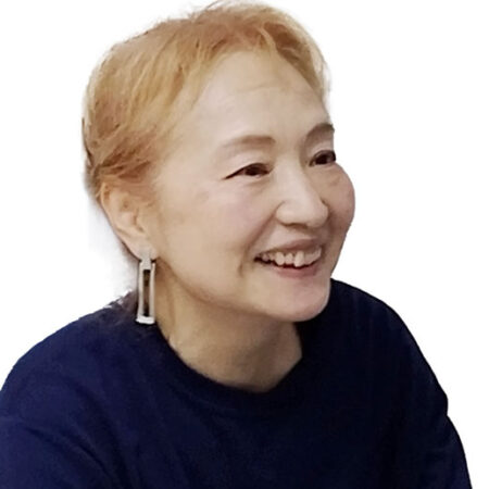 Smiling woman with short blond hair, wearing a dark blue top and rectangular drop earrings, facing slightly to the right.