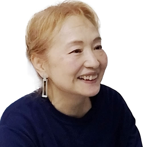 Smiling woman with short blond hair, wearing a dark blue top and rectangular drop earrings, facing slightly to the right.